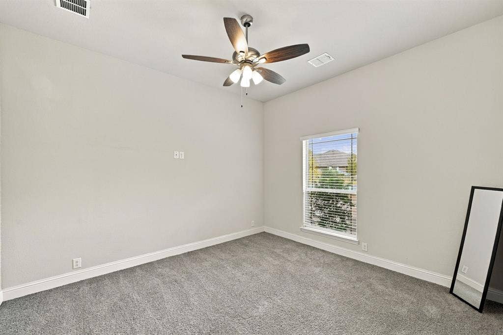 Plush gray carpeting, a window with blinds, and a ceiling fan with integrated lighting