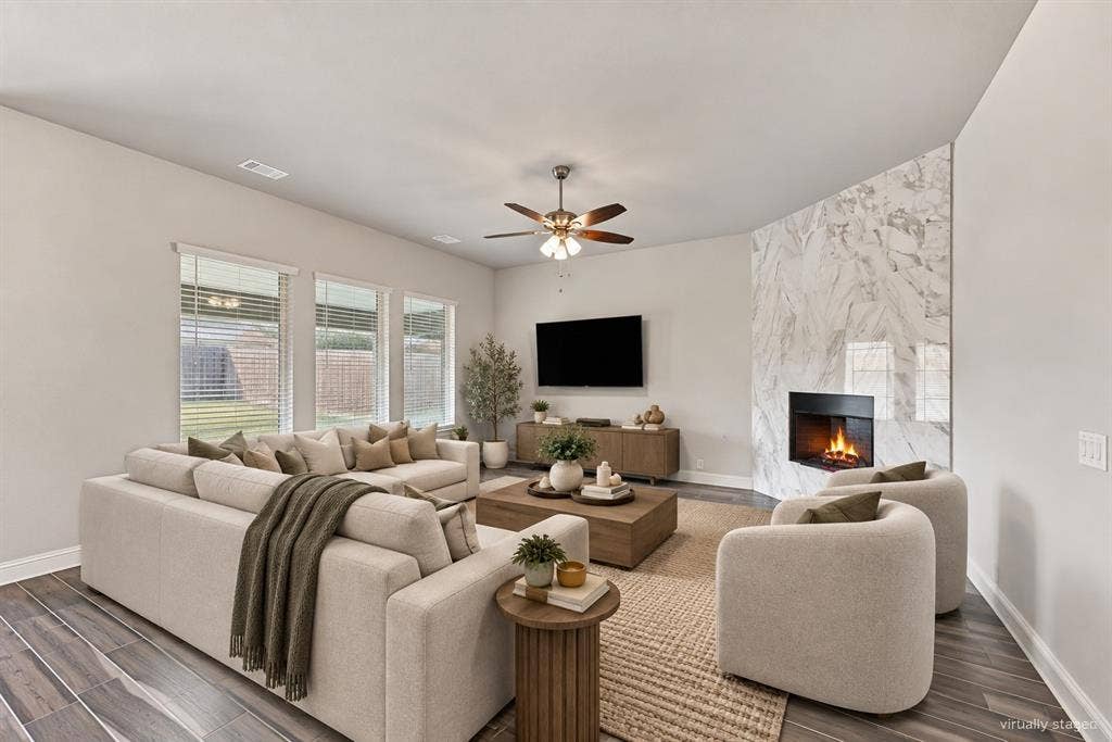 Spacious living area featuring wood-finish flooring, a contemporary fireplace with a stone surround, and multiple windows providing natural light
