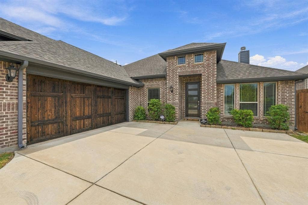 Brick exterior with a prominent entry, large front windows, a full concrete driveway, and a multi-car wooden garage door