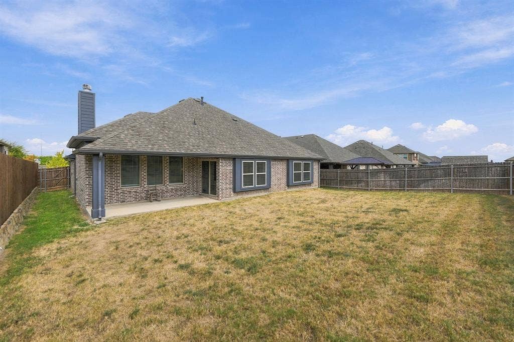 Brick exterior with dark trim windows, covered patio, sliding glass door, and a fully fenced backyard