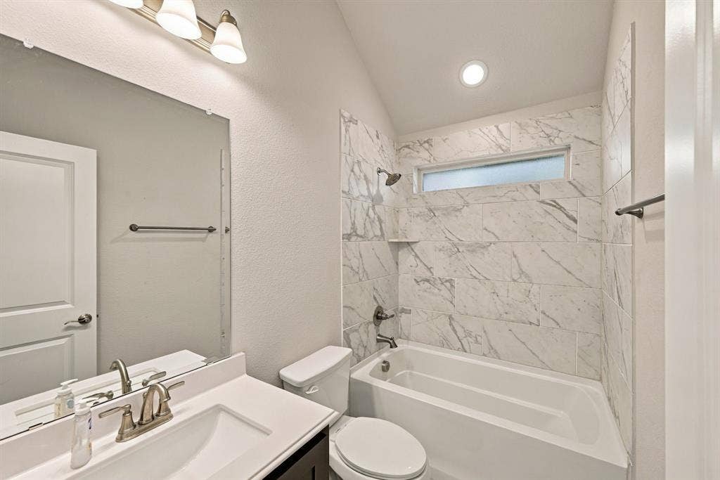 Full bathroom featuring a single vanity, a built-in tub with a shower, a large wall mirror, and modern overhead lighting