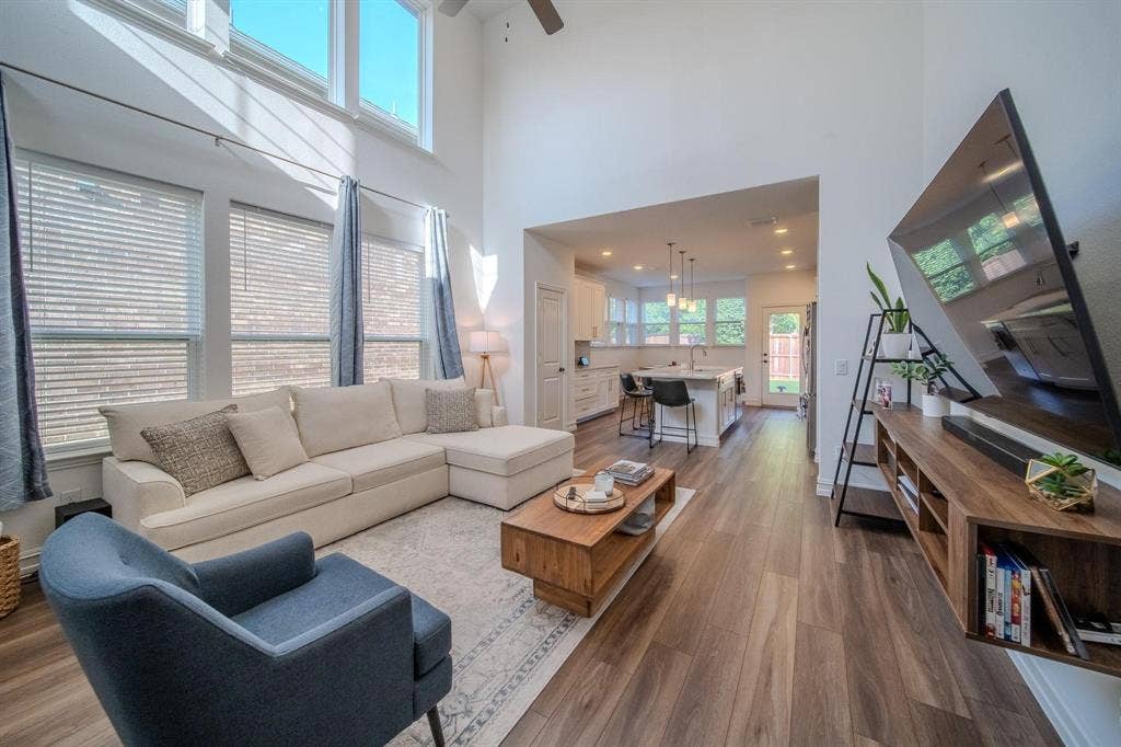 4629 Golden Gate Way, Garland, TX 75043 Two-story living area with high ceilings and expansive windows, wood-finish flooring, and a kitchen with an island and pendant lighting