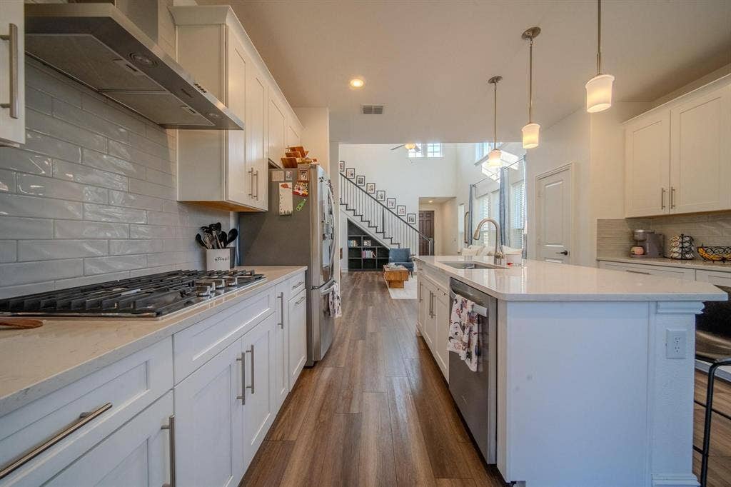 4629 Golden Gate Way, Garland, TX 75043 Kitchen featuring white shaker cabinetry, light-toned countertops, a gas range with stainless steel hood, a large kitchen island with pendant lighting, and wood-finish flooring