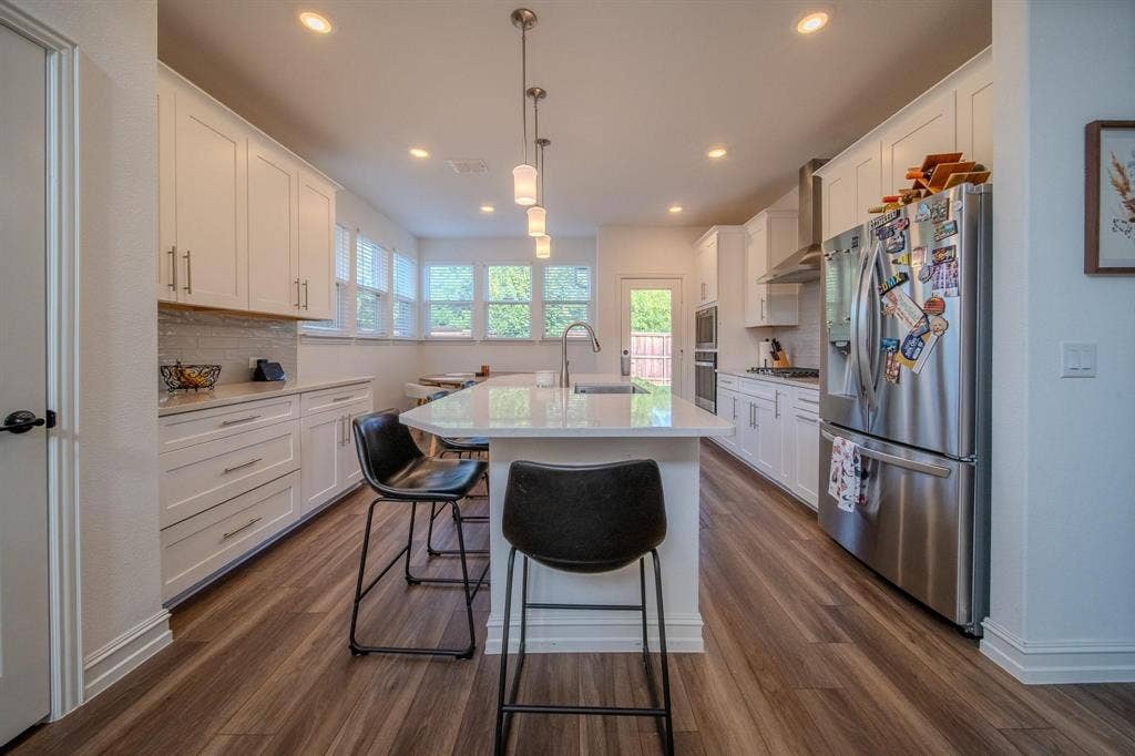 4629 Golden Gate Way, Garland, TX 75043 Gourmet kitchen with wood-finish flooring, white cabinetry, a large island with seating, pendant lighting, and stainless steel appliances
