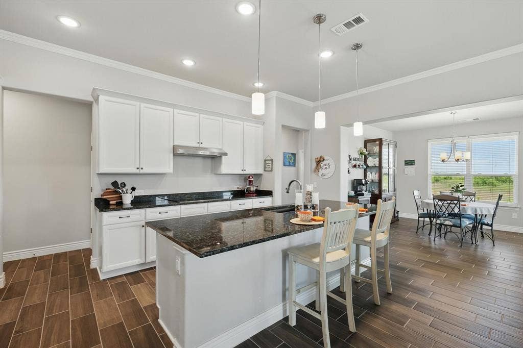 Eat in kitchen with bar, under cabinet  range hood, and black electric cook top.