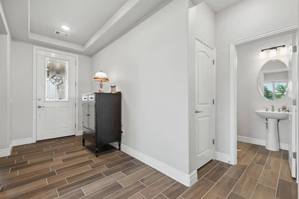 Foyer entrance featuring wood-look ceramic tiled floors, a tray ceiling. and powder bath with pedestal sink.