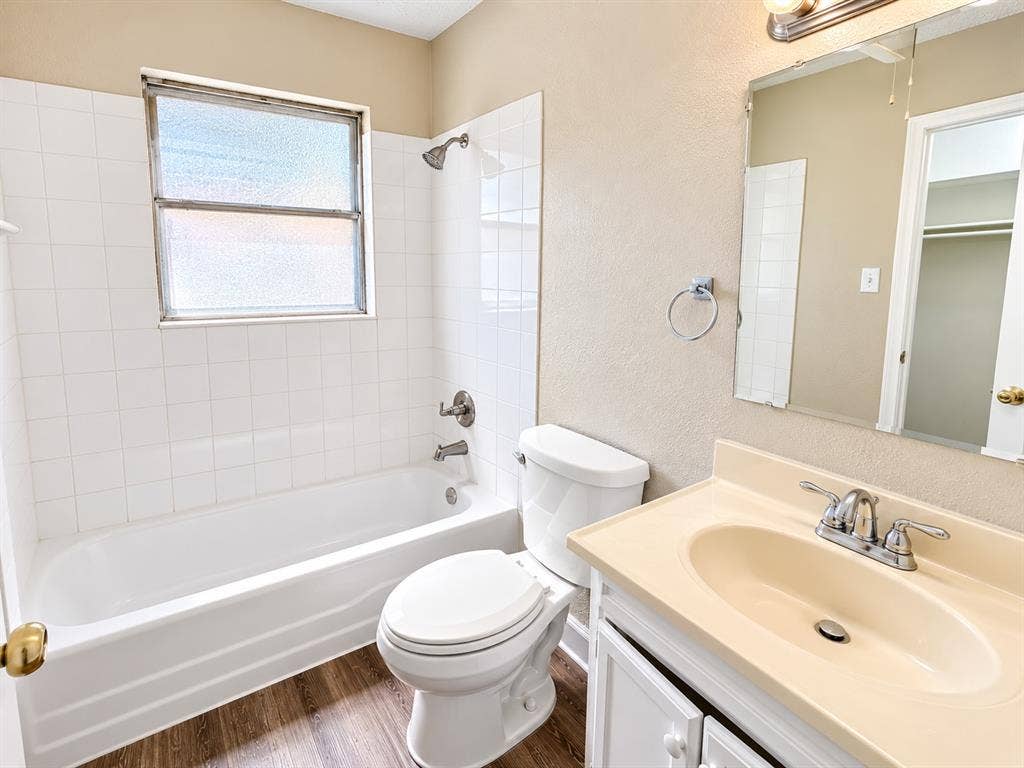 1500 Sherrye Drive, Plano, TX 75074 Bathroom featuring a single vanity, wood-finish flooring, a toilet, a tub, and tiled shower walls