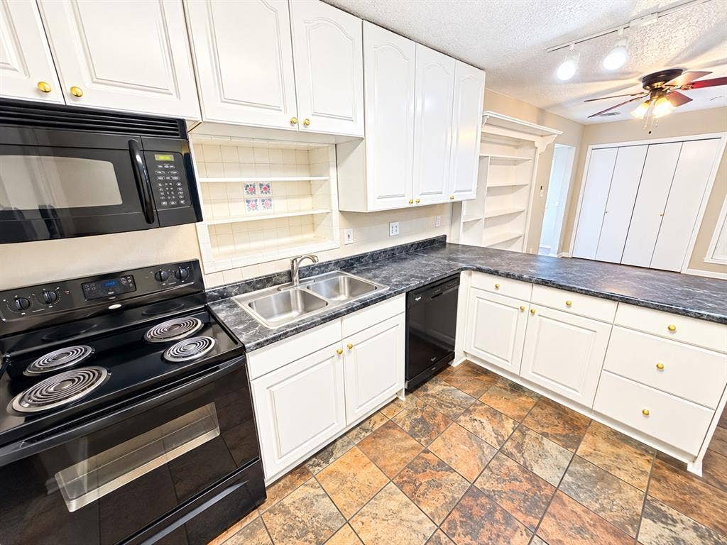 1500 Sherrye Drive, Plano, TX 75074 White cabinetry with gold-tone hardware, black appliances, double basin stainless steel sink, dark patterned countertops, and multi-toned tile flooring