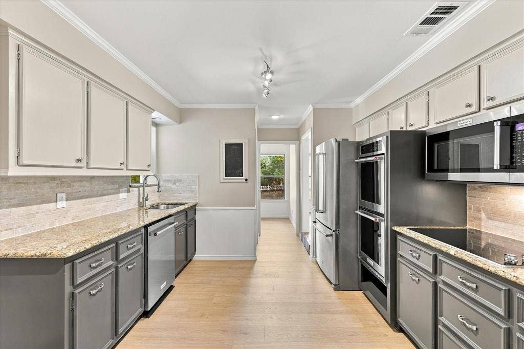 2811 Reedcroft Drive, Farmers Branch, TX 75234 Well-appointed kitchen featuring dual-tone cabinetry, stone countertops, stainless steel appliances, and wood-finish flooring