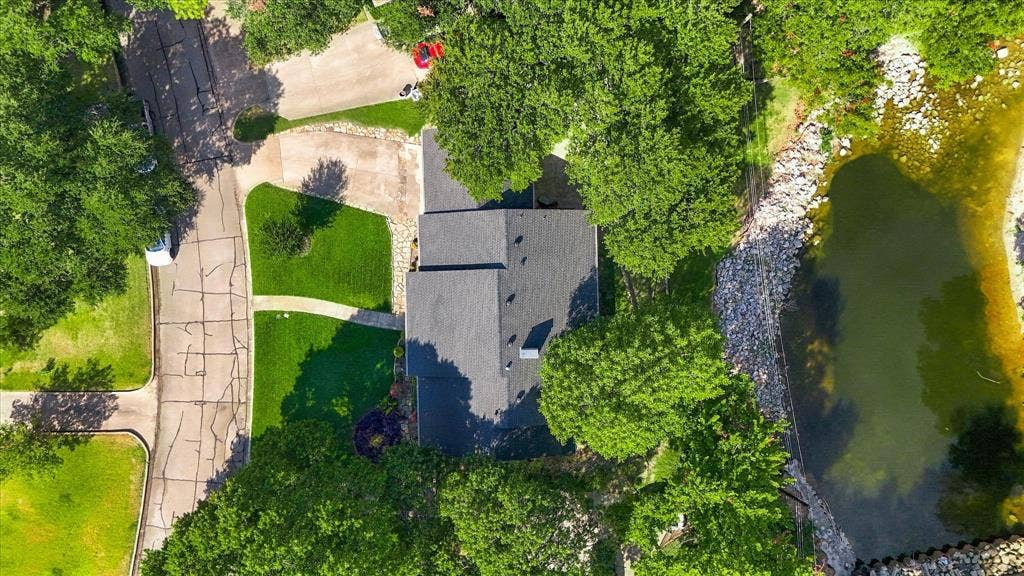2811 Reedcroft Drive, Farmers Branch, TX 75234 Manicured lawn with mature trees, paved driveways, and a river frontage with stone-lined banks