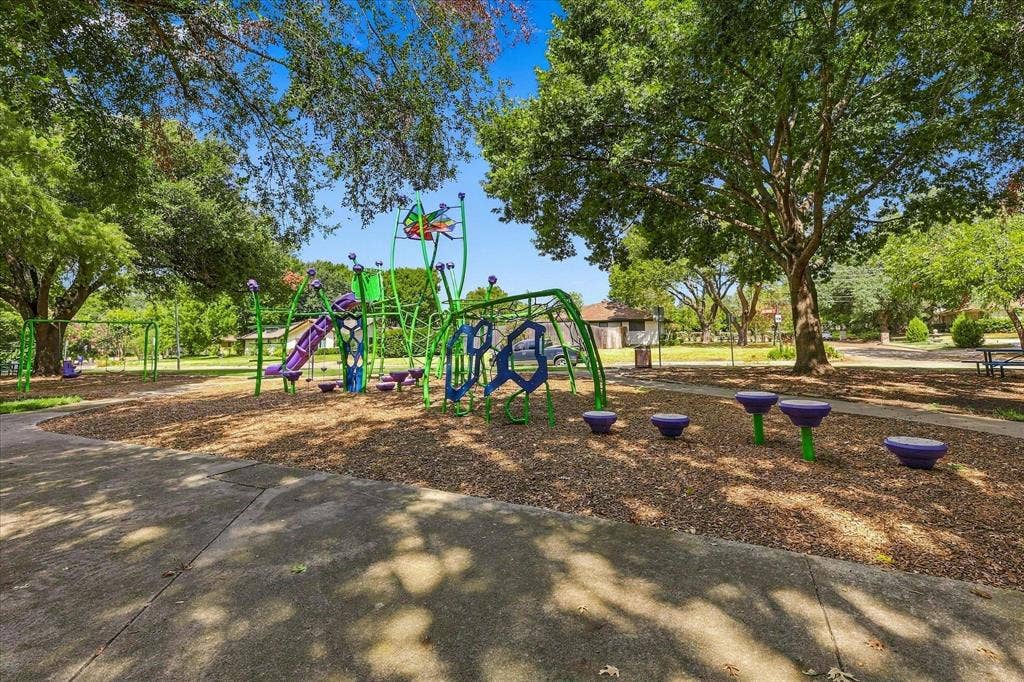 2811 Reedcroft Drive, Farmers Branch, TX 75234 Community playground with diverse play equipment, including slides, swings, and climbing structures, set on a wood chip surface, surrounded by mature trees
