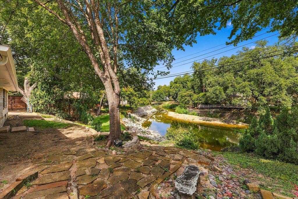 2811 Reedcroft Drive, Farmers Branch, TX 75234 Stone patio with a natural rock edge, mature trees, and a bordering water feature