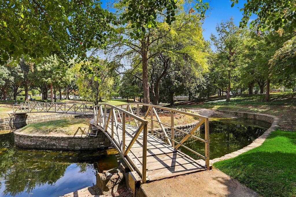 2811 Reedcroft Drive, Farmers Branch, TX 75234 Landscaped grounds featuring a footbridge over water, surrounded by mature trees and lush greenery