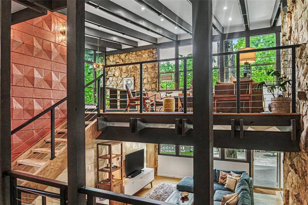 11737 Rogue Way, Dallas, TX 75218 Multi-level interior featuring exposed steel beams, floor-to-ceiling natural stone wall, decorative geometric masonry, cable-railing staircase, and expansive window walls