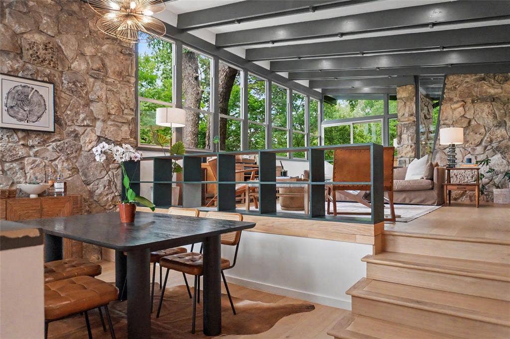 11737 Rogue Way, Dallas, TX 75218 Natural stone accent walls, exposed ceiling beams, expansive floor-to-ceiling windows, light wood-finish flooring, and built-in grid shelving