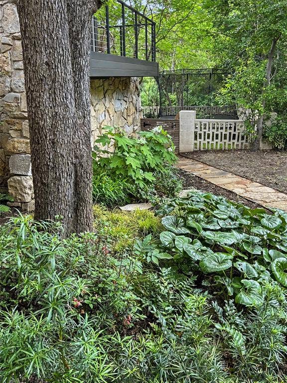 11737 Rogue Way, Dallas, TX 75218 Natural stone exterior wall, elevated deck with dark metal railings, flagstone walkway, and mature native landscaping