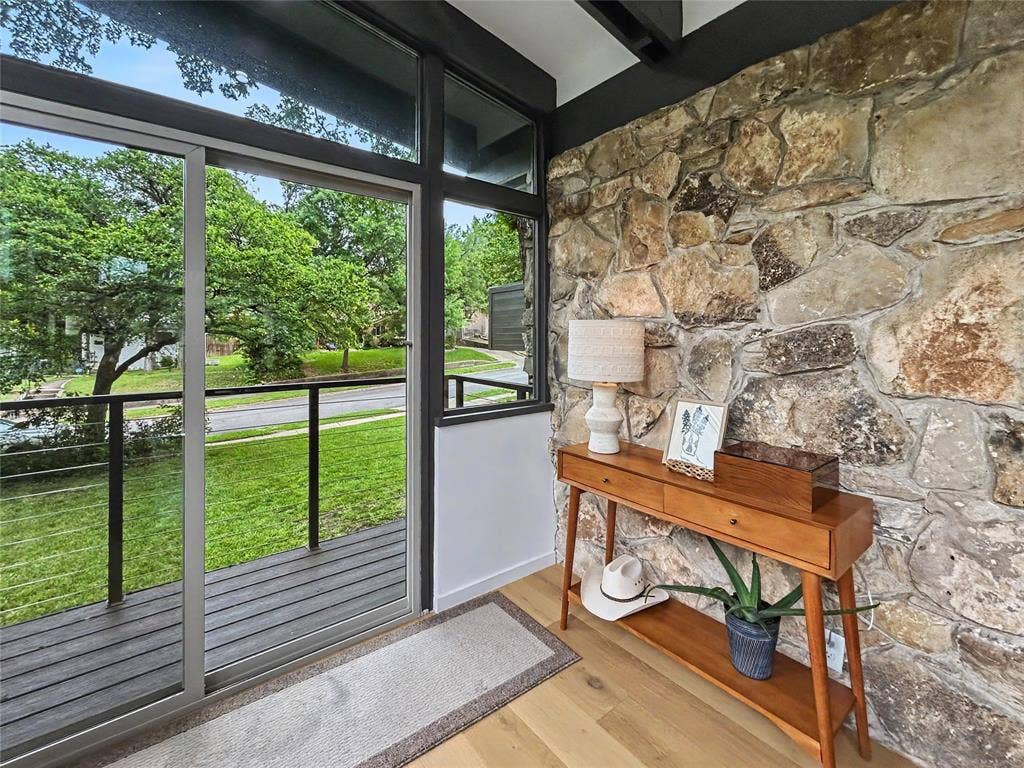 11737 Rogue Way, Dallas, TX 75218 Stacked stone accent wall, hardwood flooring, and floor-to-ceiling wall of windows opening up to one of many balconies