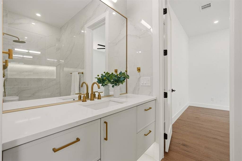 6911 Mohawk, Dallas, TX 75235 Double vanity with integrated sinks, gold-finish fixtures, and a large framed mirror