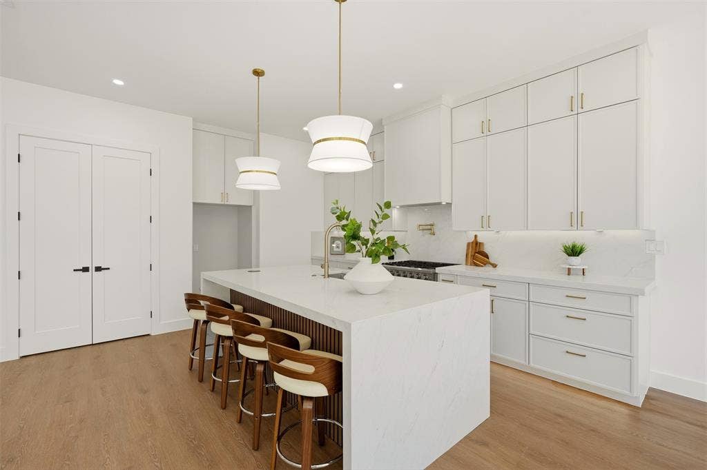 6911 Mohawk, Dallas, TX 75235 Central kitchen island with a waterfall countertop, brass hardware, wood-finish flooring, and white cabinetry