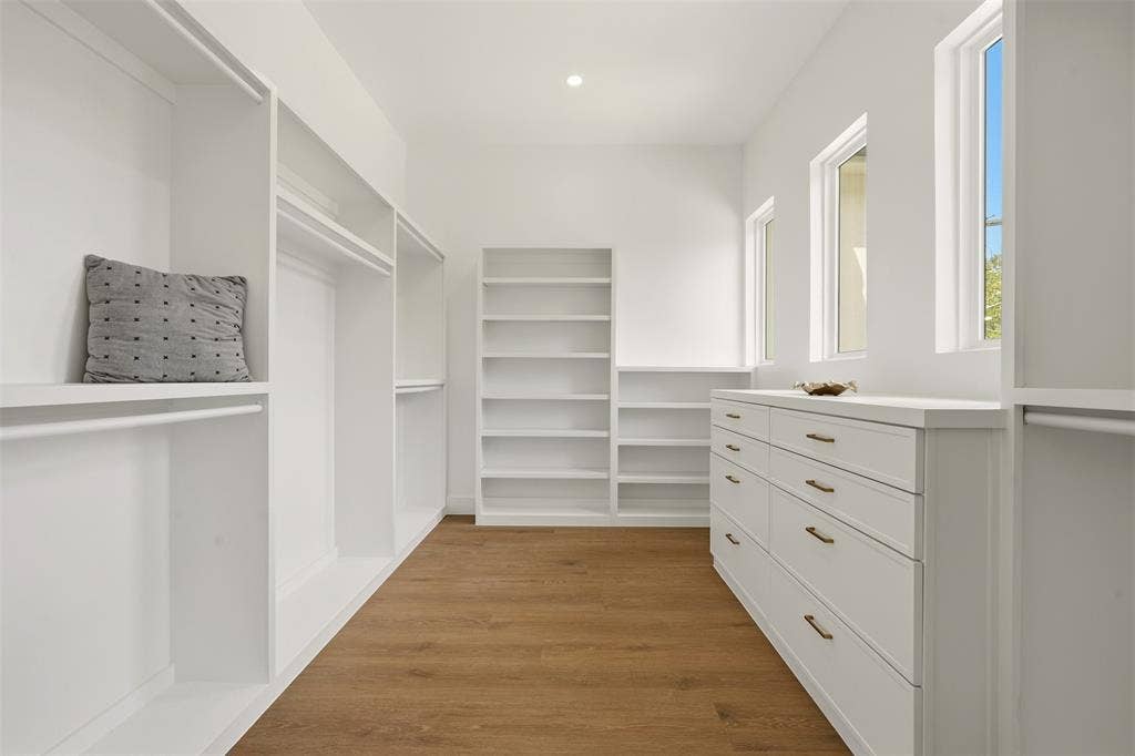 6911 Mohawk, Dallas, TX 75235 Spacious closet with wood-finish flooring, white built-in shelving, white built-in cabinetry with bronze hardware, and multiple windows