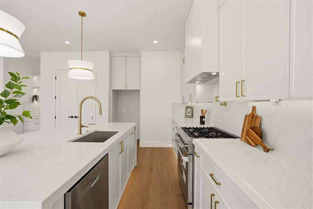 6911 Mohawk, Dallas, TX 75235 White shaker cabinetry with gold-tone hardware, stainless steel appliances, a kitchen island with an undermount sink, and wood-finish flooring