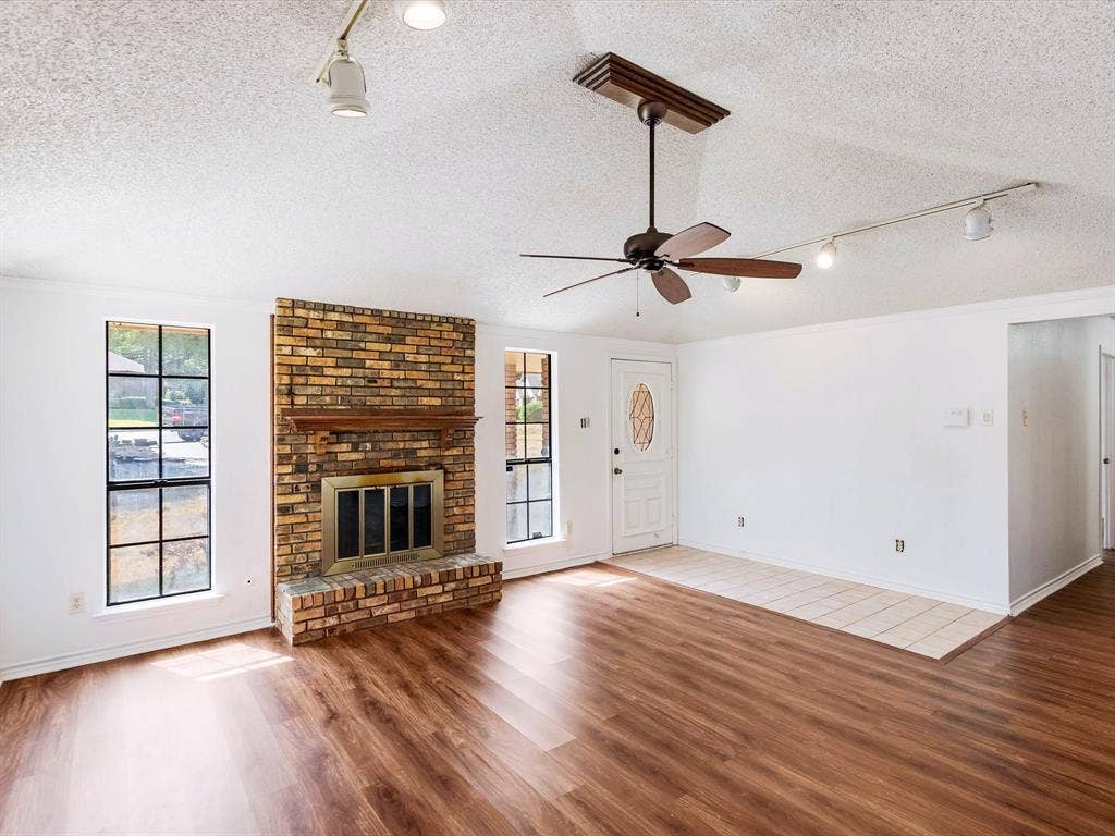 219 N Beltwoods Drive, DeSoto, TX 75115 Spacious room featuring wood-finish flooring, a brick fireplace with a wood mantle, and multiple grid-pattern windows