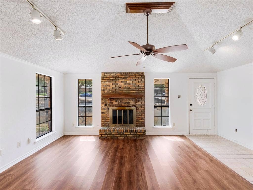 219 N Beltwoods Drive, DeSoto, TX 75115 Wood-finish flooring throughout, brick fireplace with wood mantel, ceiling fan, track lighting, and a front entry door with decorative glass inlay