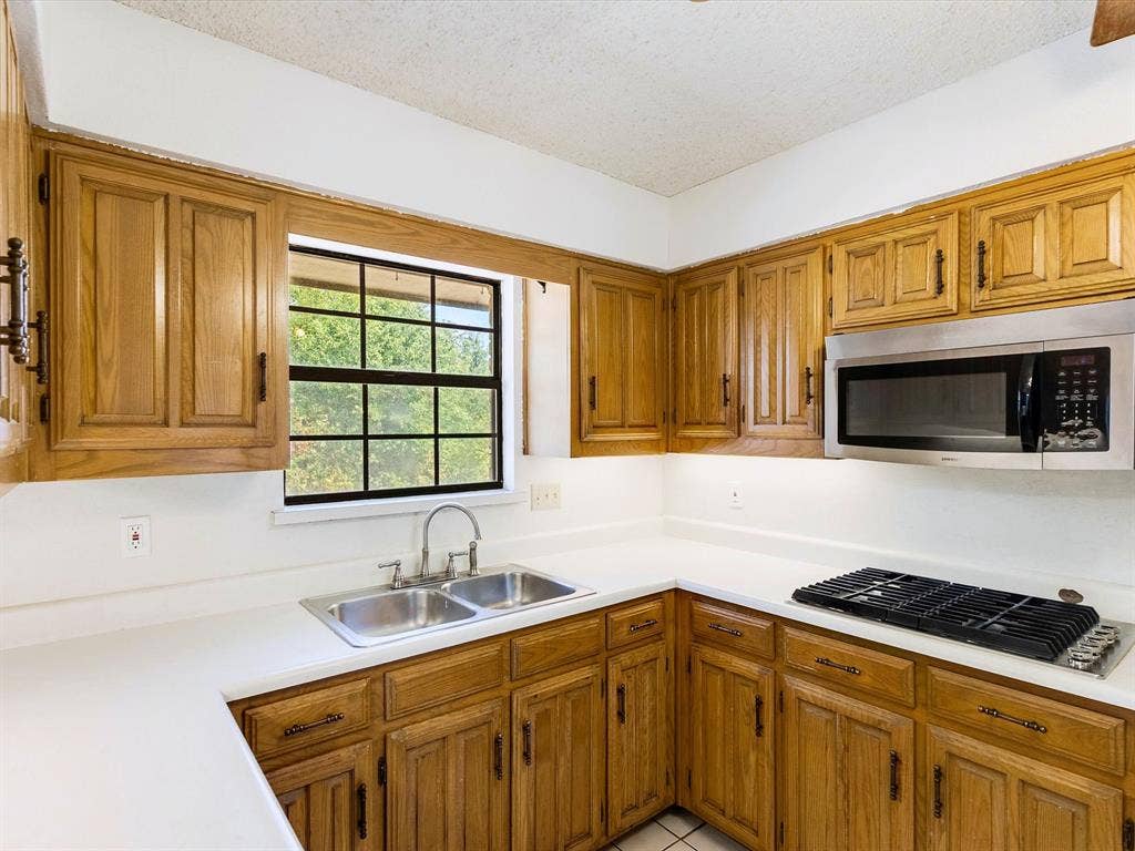 219 N Beltwoods Drive, DeSoto, TX 75115 Kitchen with wood cabinetry, white countertops, stainless steel dual basin sink, and an over-range microwave