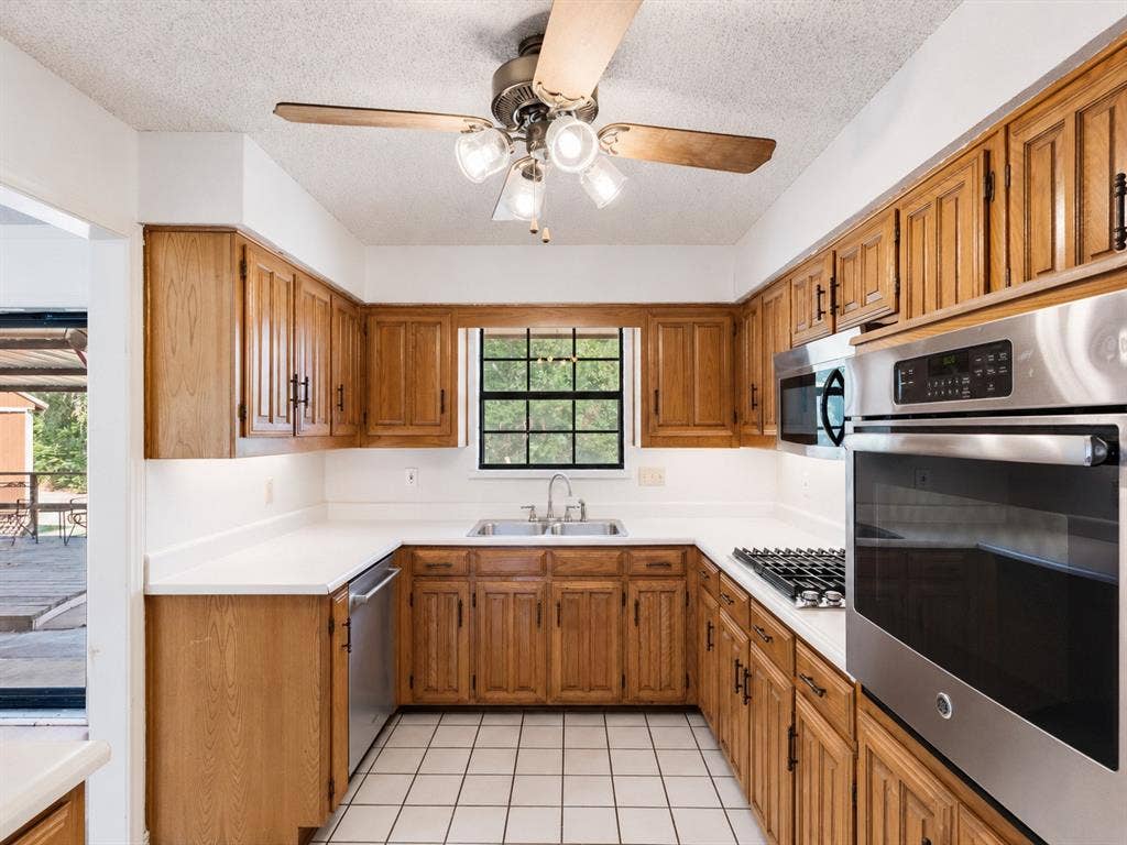 219 N Beltwoods Drive, DeSoto, TX 75115 Kitchen featuring wood-finish cabinetry, stainless steel appliances, white countertops, a ceiling fan with integrated lighting, and tile flooring