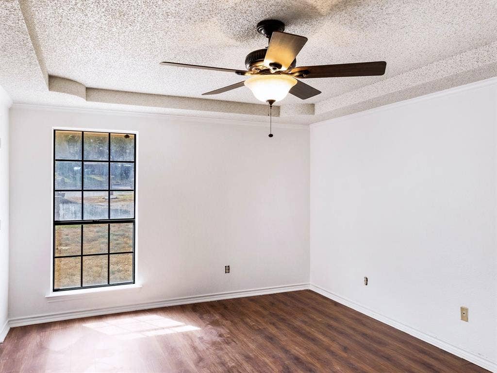 219 N Beltwoods Drive, DeSoto, TX 75115 Tray ceiling with textured finish, wood-finish flooring, ceiling fan with integrated lighting, and a multi-pane window