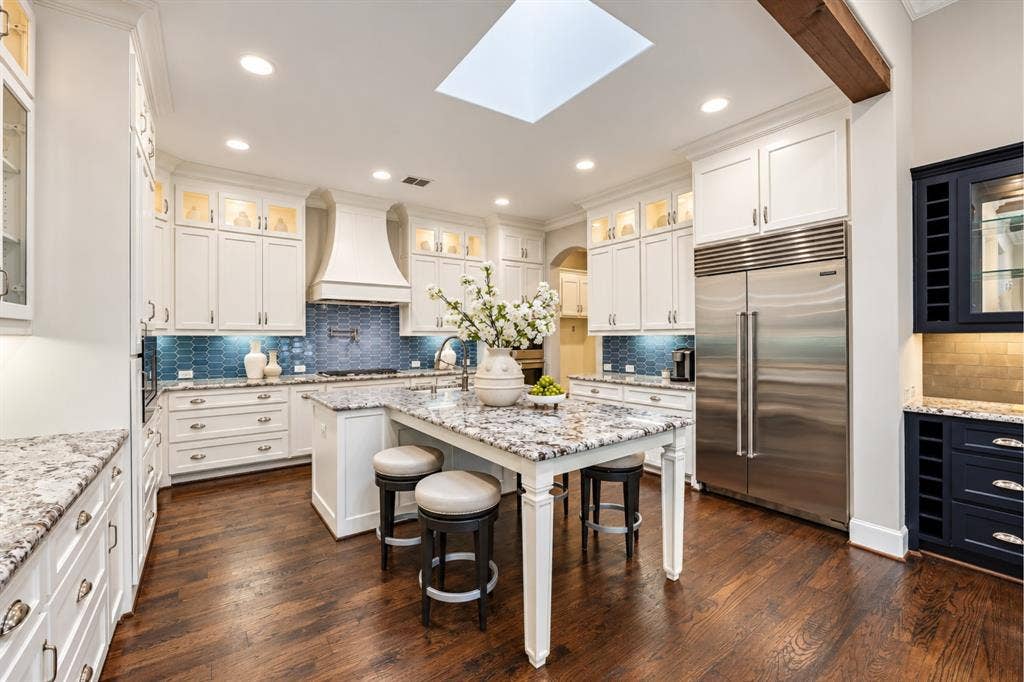 6816 Cousteau Court, Plano, TX 75024 Gourmet kitchen featuring a large central island, white cabinetry, integrated stainless steel appliances, wood-finish flooring, and a skylight