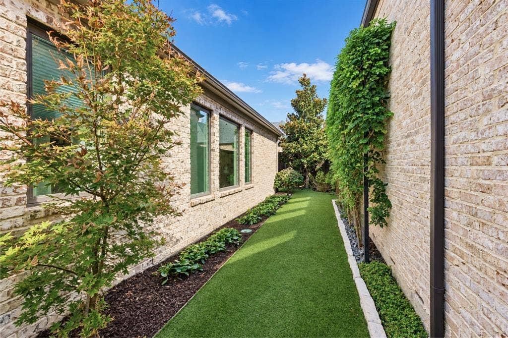 6816 Cousteau Court, Plano, TX 75024 Manicured side yard featuring artificial turf, mature tree plantings, brick exterior, and vertical wall greenery