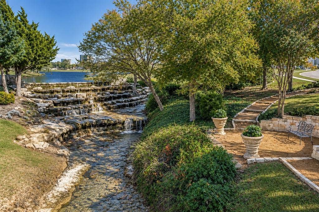 6816 Cousteau Court, Plano, TX 75024 Tiered rock waterfall with a flowing stream, stone-lined pathways, and mature trees