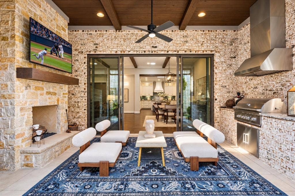 6816 Cousteau Court, Plano, TX 75024 Expansive outdoor living area featuring a stone fireplace, built-in outdoor kitchen with stainless steel appliances, wood-beamed ceiling, and a ceiling fan