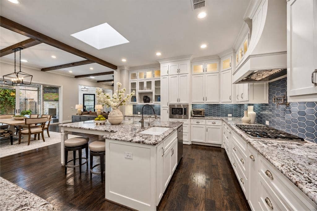 6816 Cousteau Court, Plano, TX 75024 Kitchen featuring white cabinetry, light-toned countertops, a geometric blue tile backsplash, a central island with a sink, and dark wood-finish flooring
