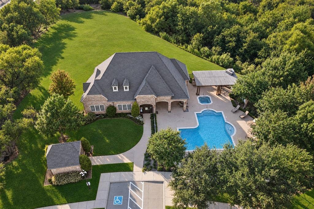 6816 Cousteau Court, Plano, TX 75024 Stone exterior featuring a dark-toned roof, dormer windows, a swimming pool, and an attached hot tub