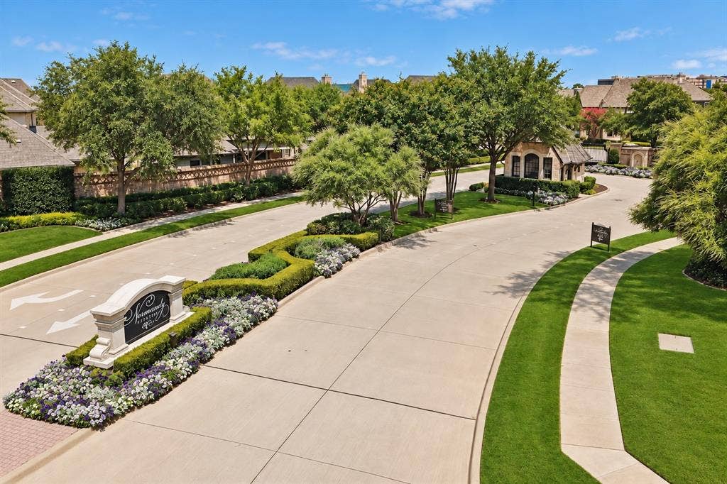 6816 Cousteau Court, Plano, TX 75024 Landscaped entryway with a stone sign, manicured lawns, mature trees, and a stone-clad gatehouse