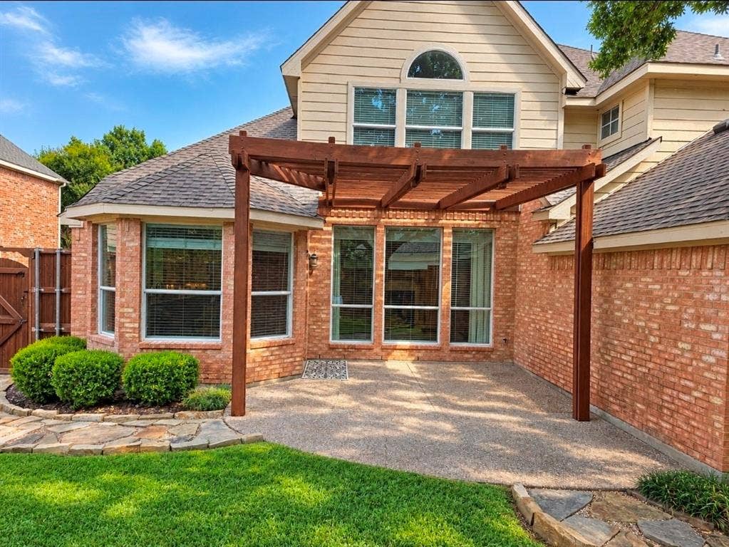 3708 Stockport Drive, Plano, TX 75025 Brick exterior with a wood pergola, expansive windows, exposed aggregate patio, and a stone-lined garden bed