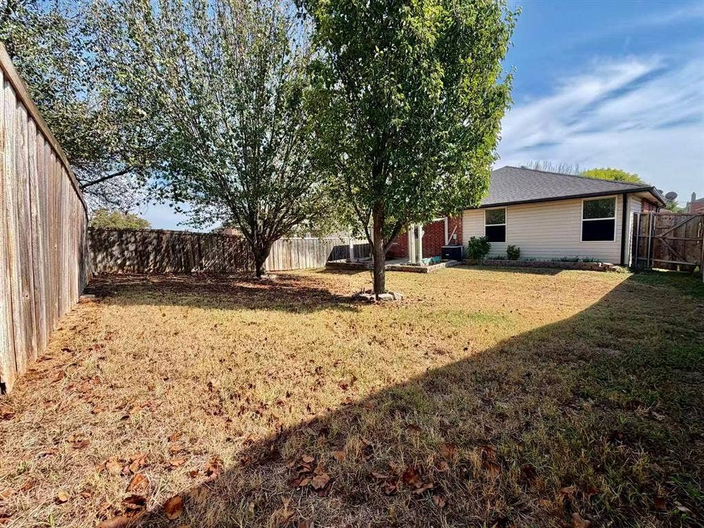 Expansive backyard featuring mature trees, wood fence perimeter, and a contemporary single-story exterior