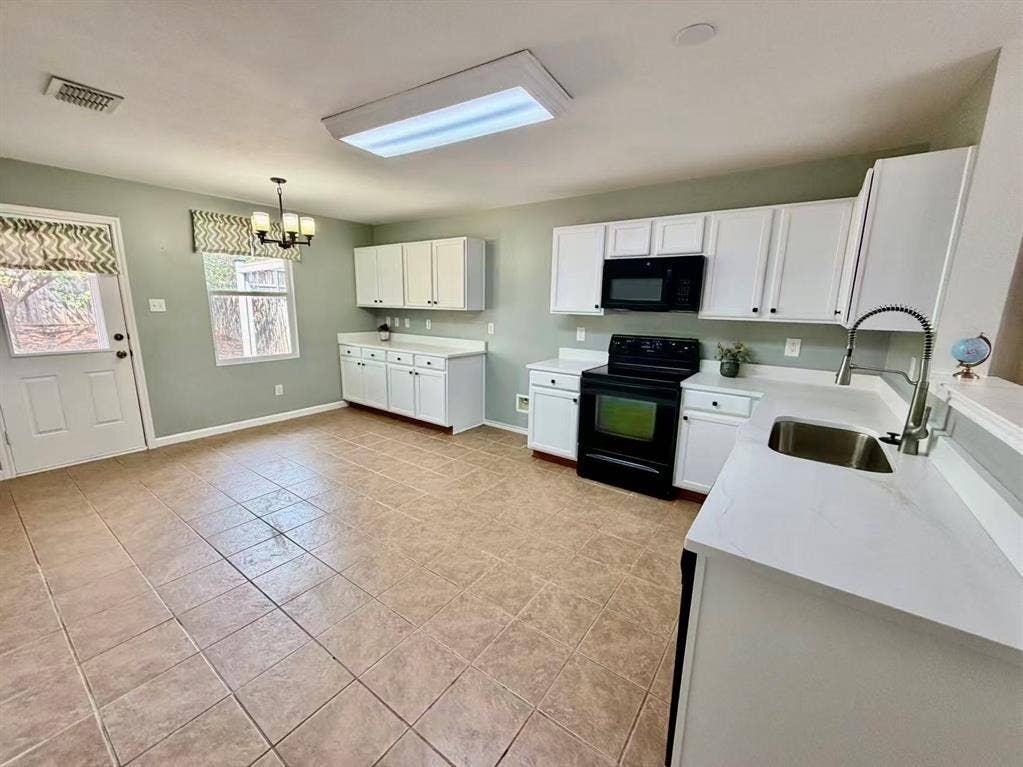 White cabinetry with black hardware, black appliances, light-toned tile flooring, and light-toned countertops