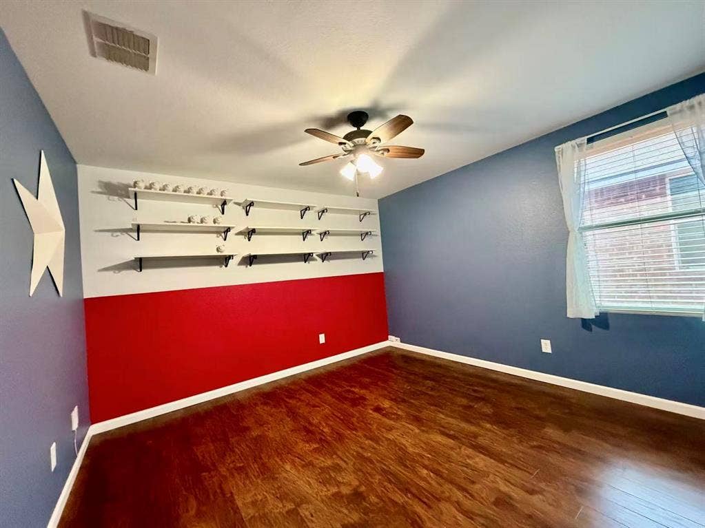 Wood-finish flooring, ceiling fan with integrated lighting, window with blinds, and built-in shelving