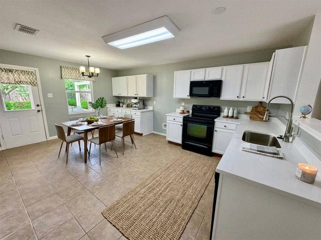 White cabinetry with black hardware, stainless steel sink with a pull-down faucet, black range, and quartez countertops, virtual staged