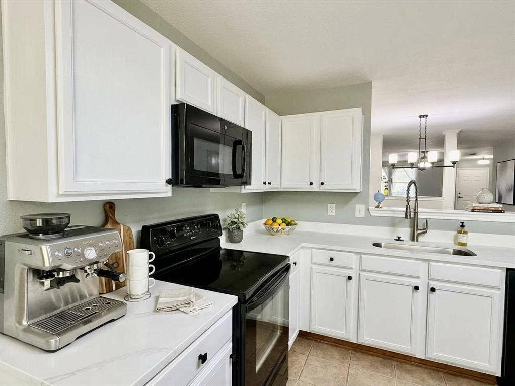 White cabinetry with black hardware, white countertops, built-in microwave, and stainless steel sink with a gooseneck faucet, virtual staged
