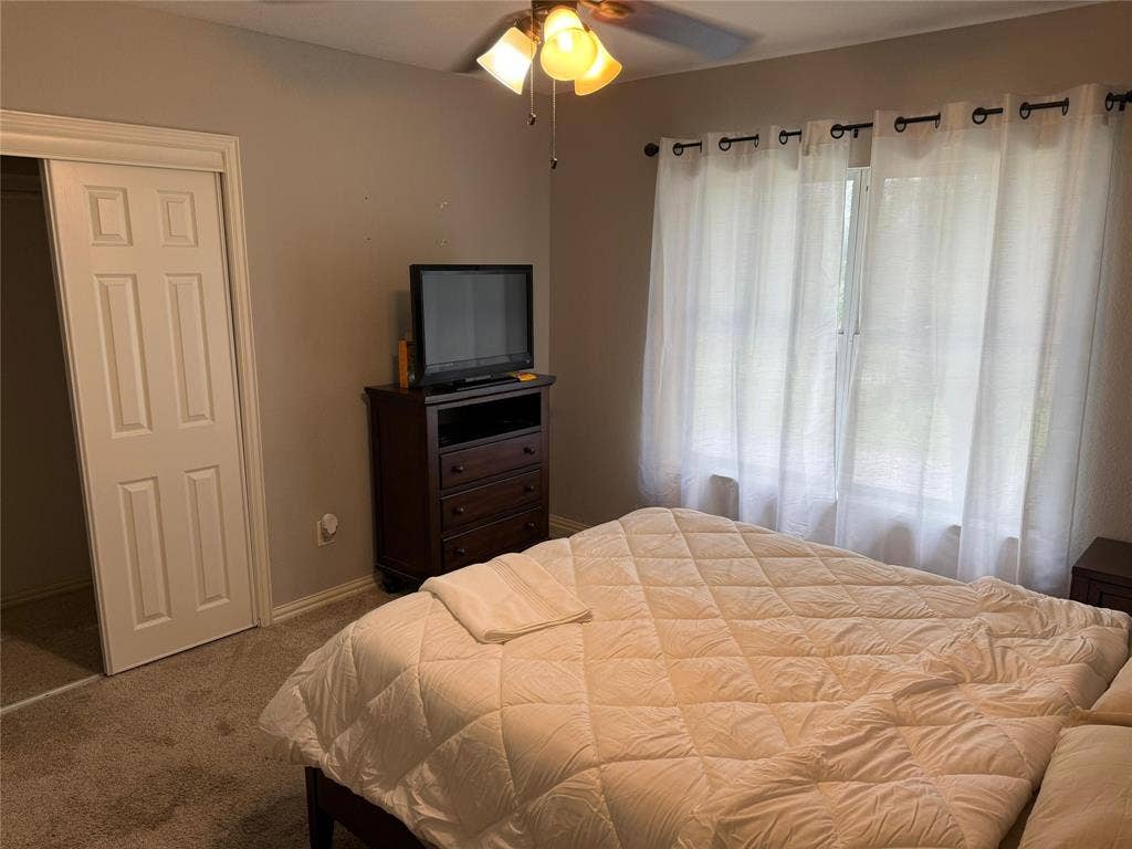 Carpeted flooring, ceiling fan with light fixture, window with drapes, and a sliding panel door