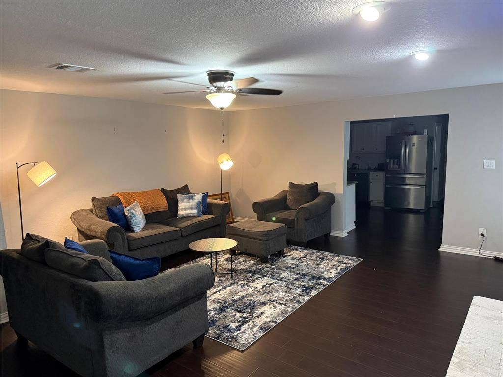 Spacious living area featuring dark wood-finish flooring, ceiling fan with integrated lighting, and recessed ceiling lights