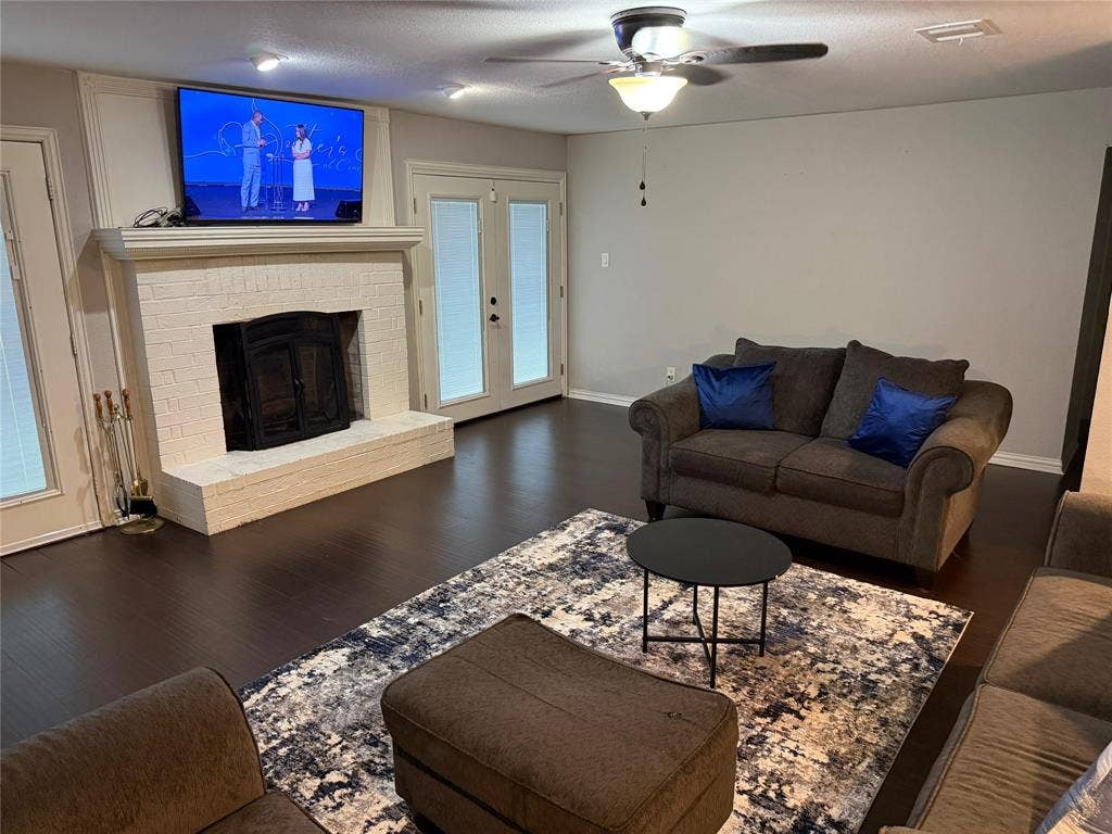 Living area featuring wood-finish flooring, a white brick fireplace, and dual French doors