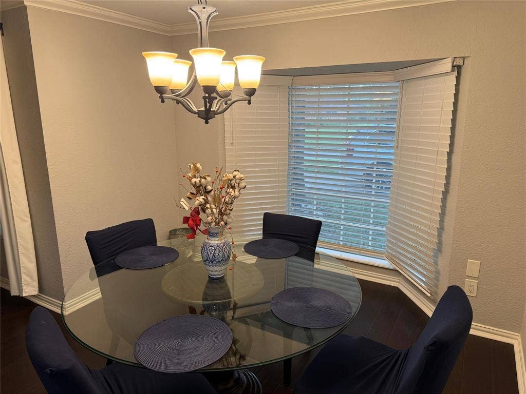 Five-light chandelier, crown molding, bay window with blinds, dark wood-finish flooring, and white baseboards