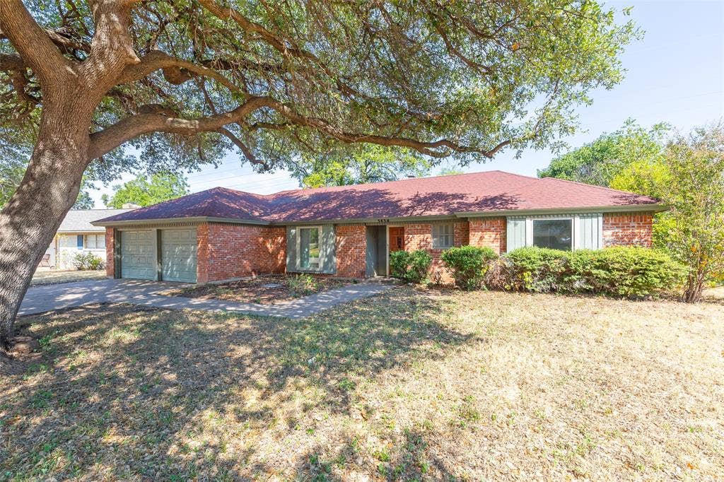 Brick exterior with a red shingle roof, featuring two garage doors, a bay window, and established landscaping