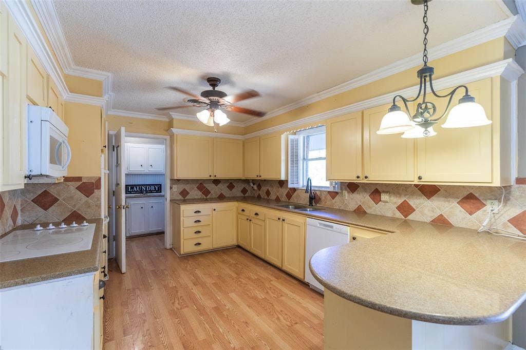 Kitchen featuring wood-finish flooring, light-toned cabinetry, built-in microwave, tile backsplash, and a ceiling fan with integrated lighting