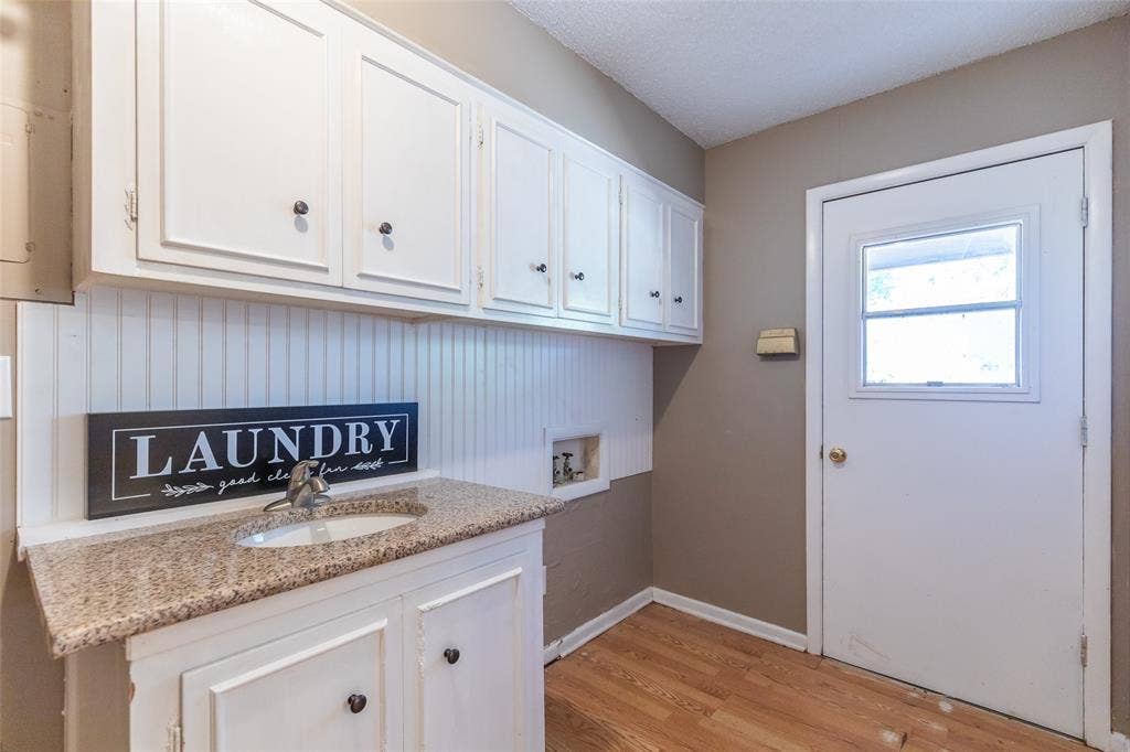 White cabinetry with black hardware, beadboard backsplash, light-toned countertop with integrated sink, and a door with a window pane
